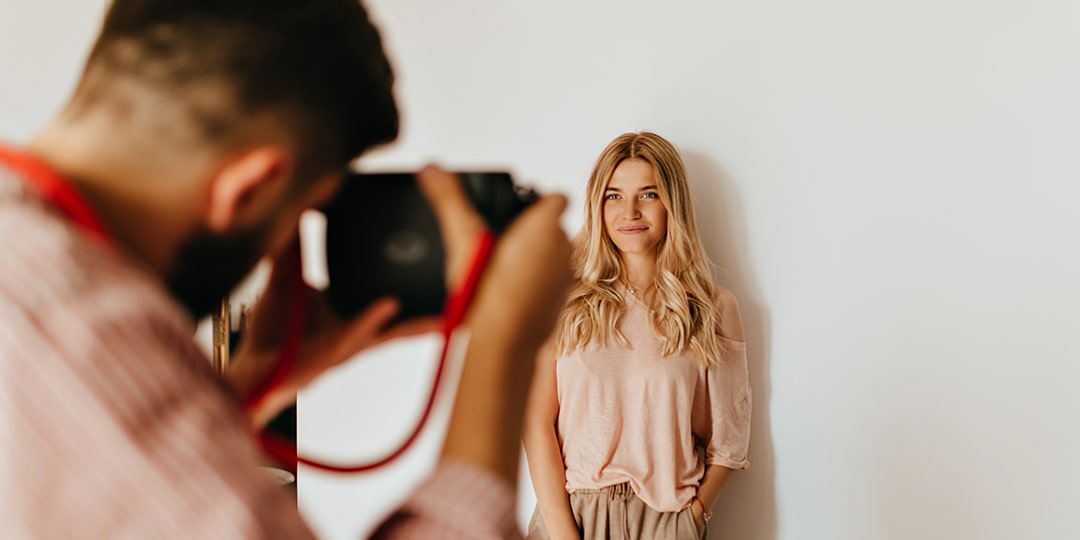 darkhaired guy makes photo his blond girlfriend dressed pink tshirt beige pants against white wall