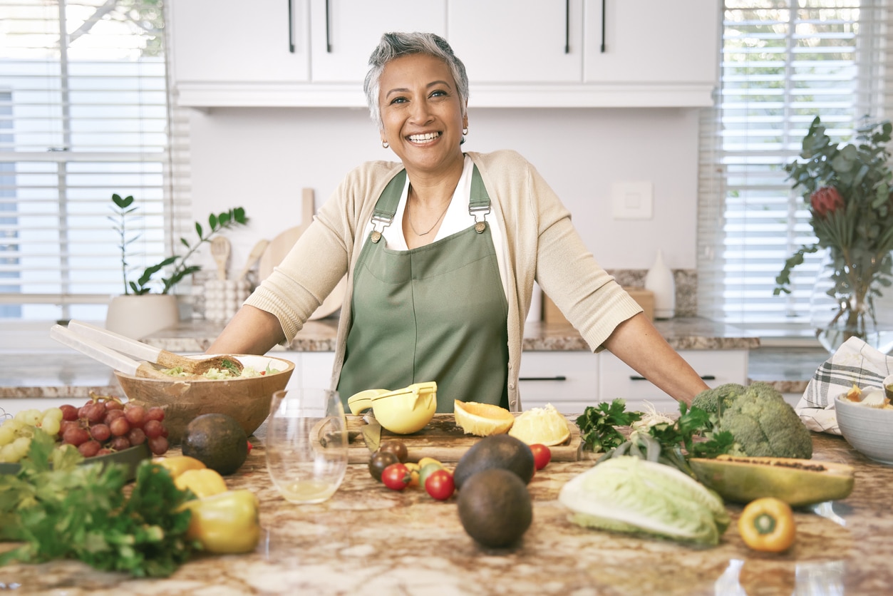 Portrait of a happy and proud mature woman in the kitchen. Standing in front of lots of veggies