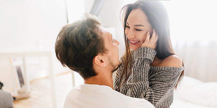 short haired happy man embracing laughing young woman gray soft clothes
