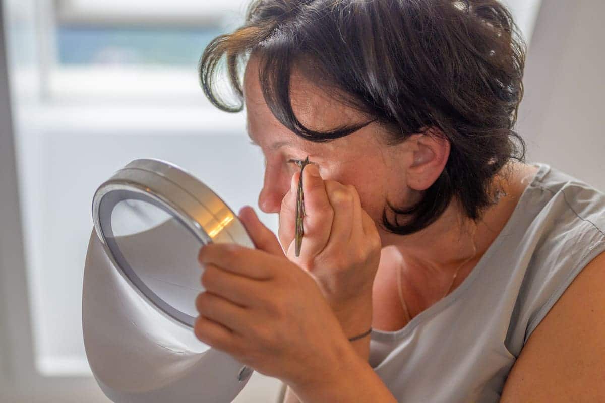 This Brow Trick Will Give You Perfect Eyebrows Everyday 2 woman plucking her eyebrows in the mirror