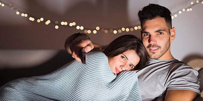 young guy with tv remote hugging lady lying sofa