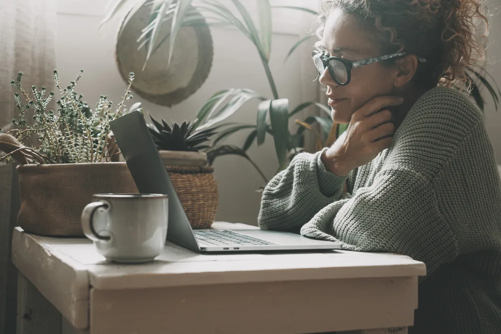 A middle age woman wearing glasses looking at her laptop reading an article on the best jobs for people with chronic illnesses