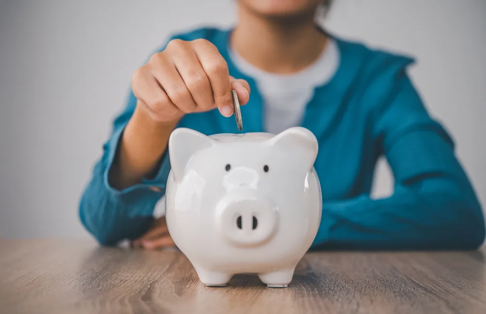 A woman putting a coin into a piggy bank for the blog post how to earn 100 a day