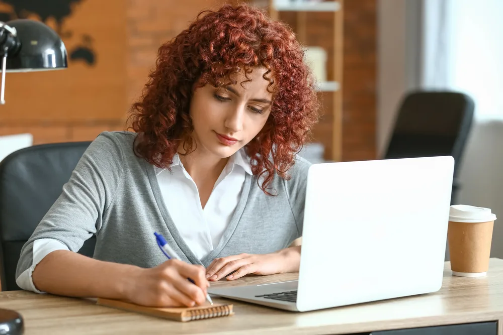 A woman with red curly hair writing in her notebook for blog post resume writers